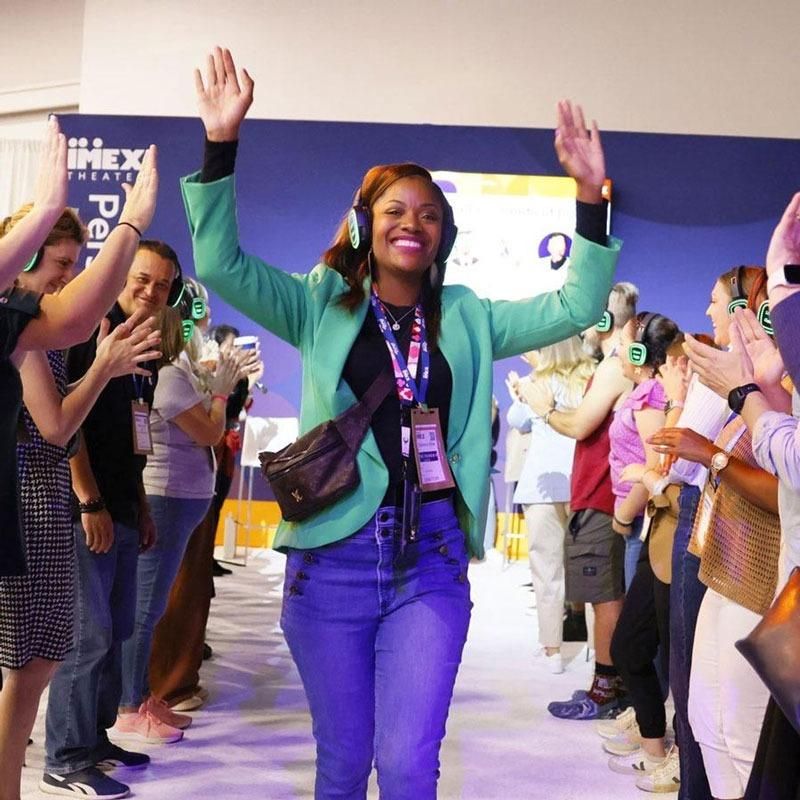 Person with hands in air walking past a crowd smiling at IMEX America