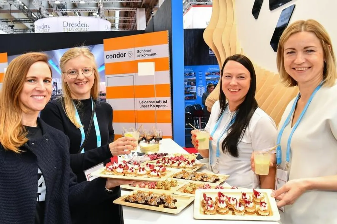 Group of four people smiling at camera with catering trays of various food and beverages