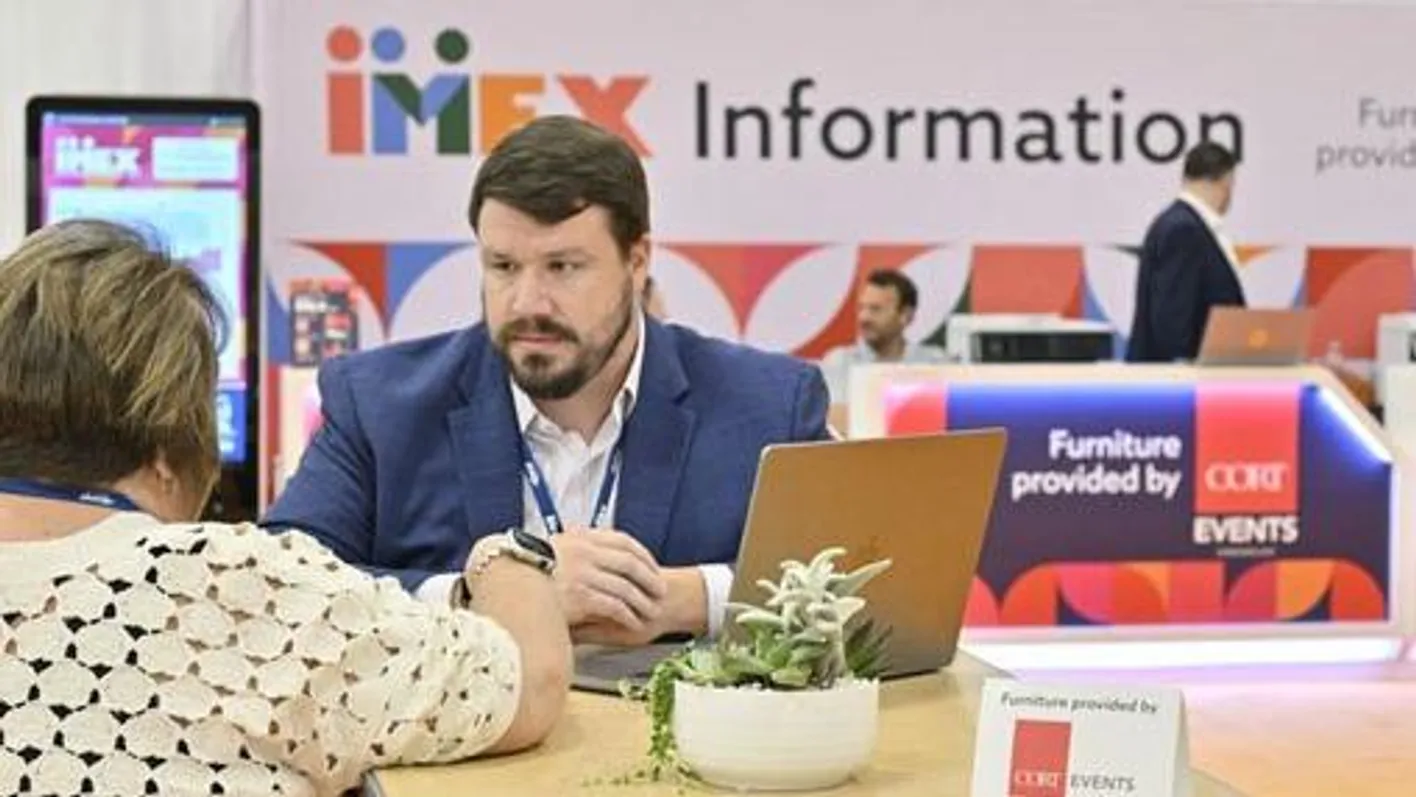 People chatting under an IMEX information sign