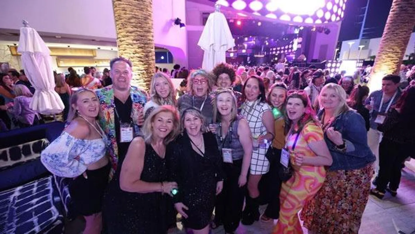 A large crowd of attendees stand smiling at the camera. They're in an outside bar.