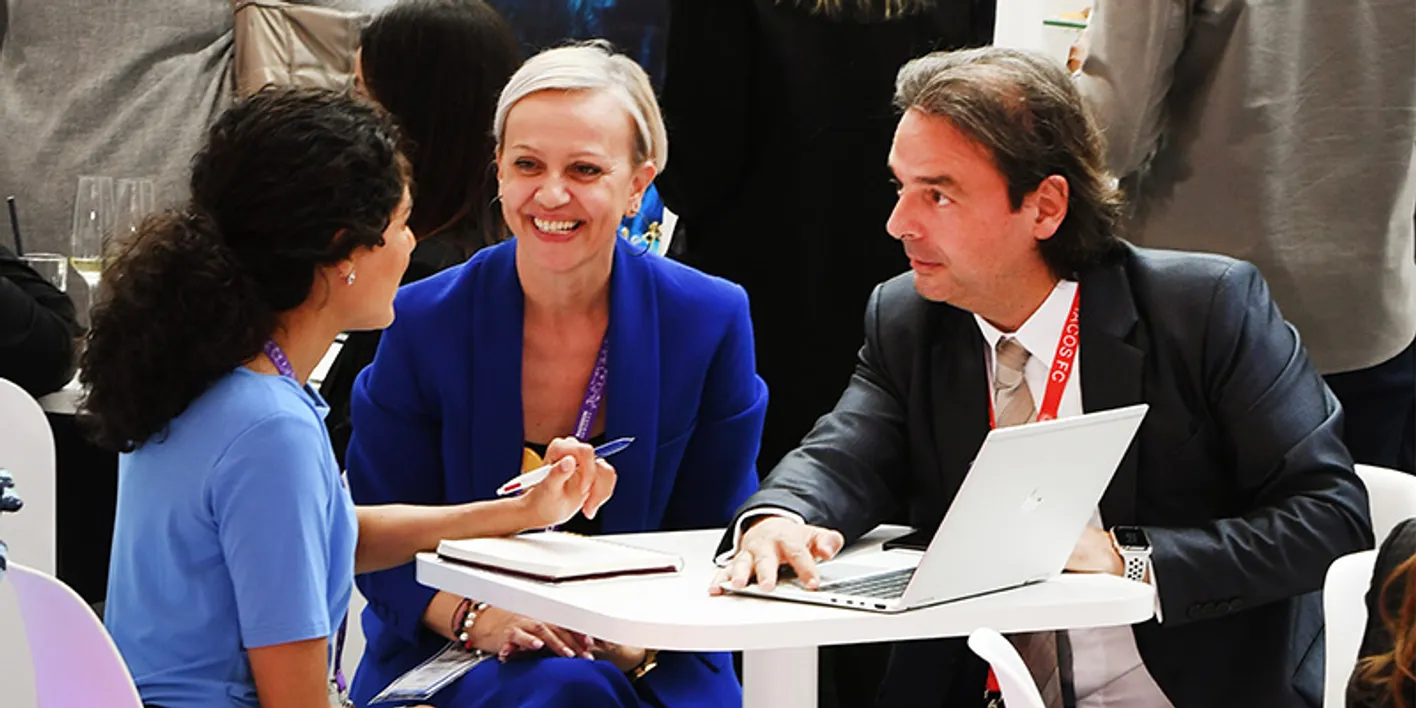 Booth partners exchanging ideas and reviewing presentations via a laptop during IMEX