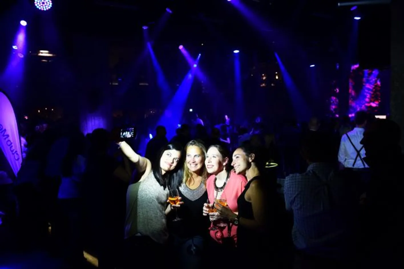 4 women taking a selfie in a nightclub. The background is dark but they are lit up by a flash photo