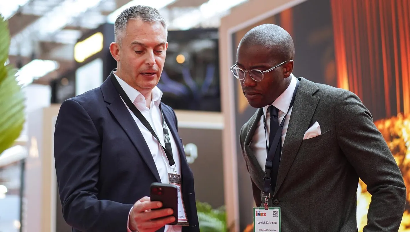 Two male professionals at IMEX Frankfurt looking at and discussing content on a smartphone.