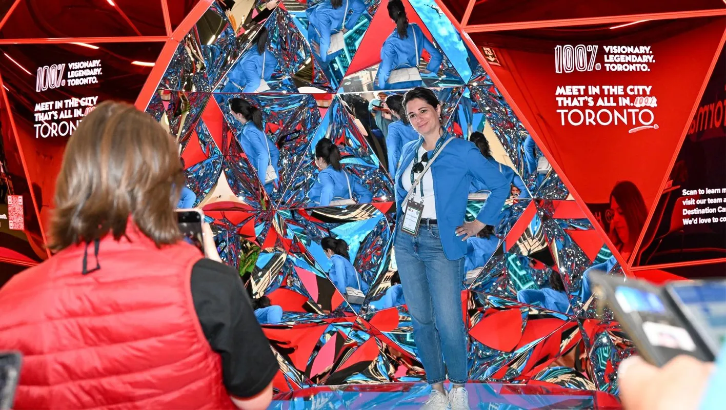 Attendee in a blue cardigan stands reflected in mirrored Toronto display as another takes a photo.