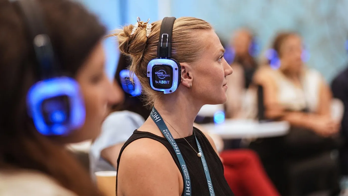 A woman with headphones on looks away from the camera, focussed on an IMEX education session. 