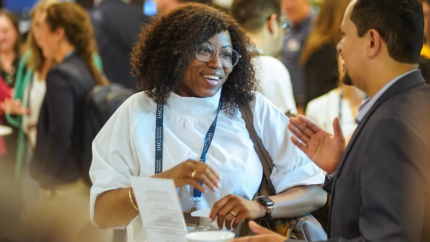 A woman stands talking and smiling to an attendee who has their back to the camera.