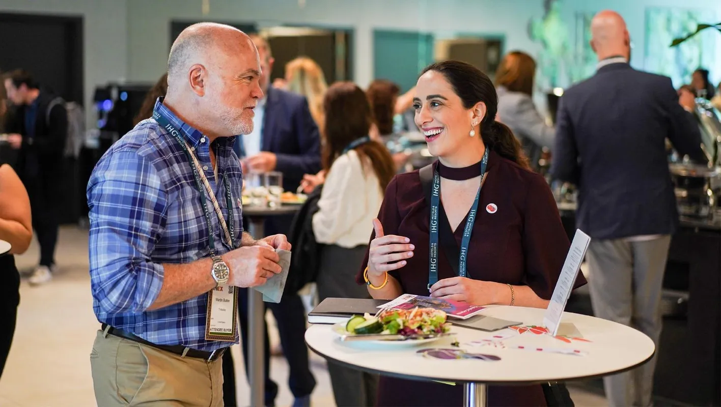 Two attendees in business casual stand at a tall table talking and laughing. 