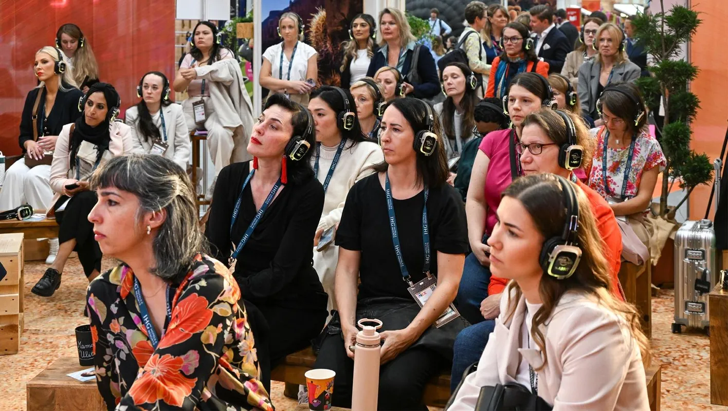A full audience listening intently to an education session. All attendees are wearing headphones.