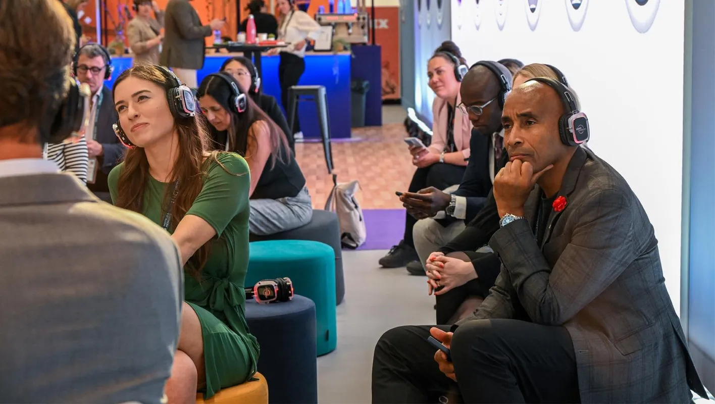 IMEX attendees sit looking beyond the camera listening to an education session, wearing headphones.
