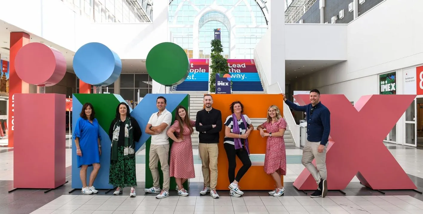 Das Vertriebsteam posiert lächelnd vor den IMEX-Buchstaben in der Gallerie. 