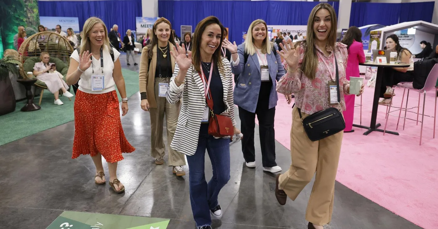 five meeting planner buyers smiling a the camera and waving in the hosted buyer lounge