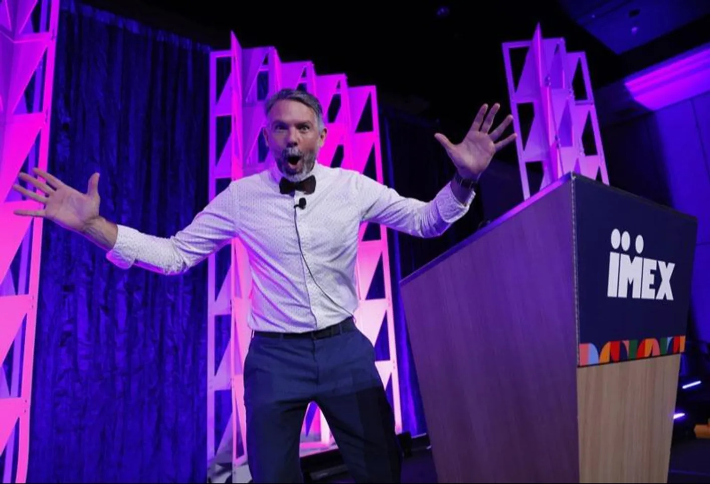 Keynote speaker onstage delivering inspiring talk with hands in the air