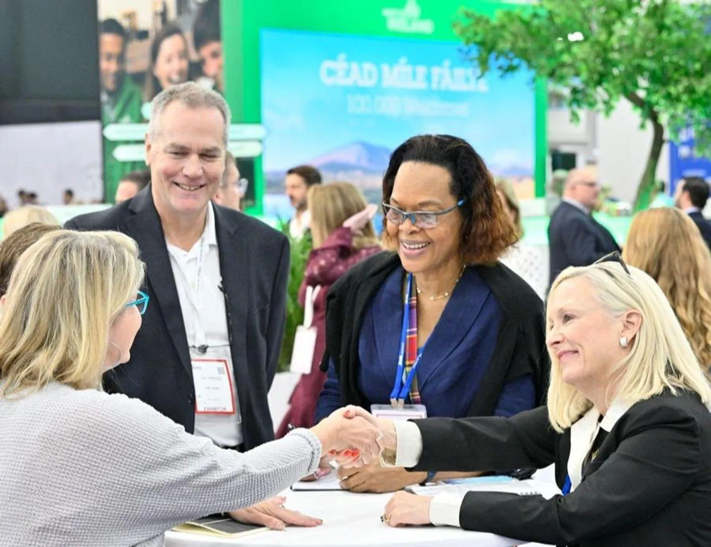 Group of meetings professionals shaking hands and smiling at a tradeshow booth