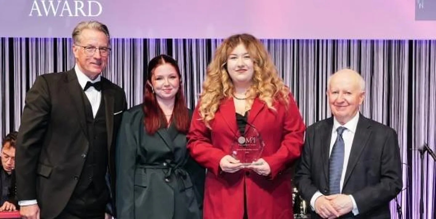 An award winner stands smiling alongside IMEX Chairman Ray Bloom and sponsors