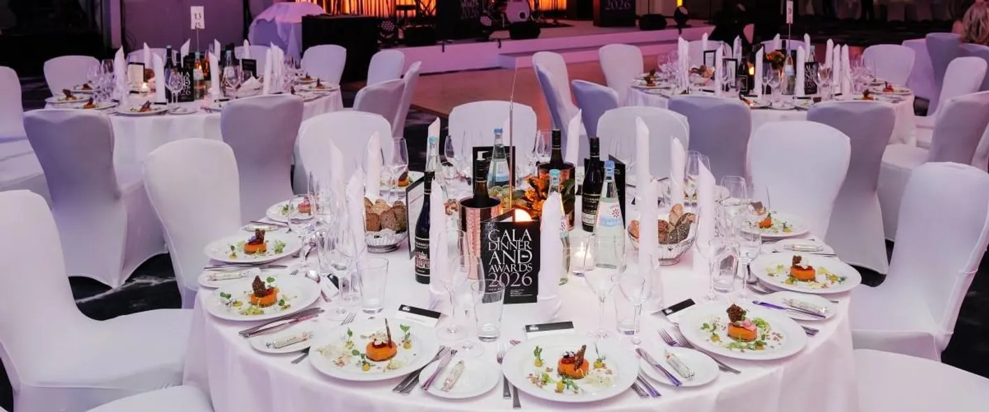 Several white roundtables set for a formal dinner. The chairs are also white. There's purple light