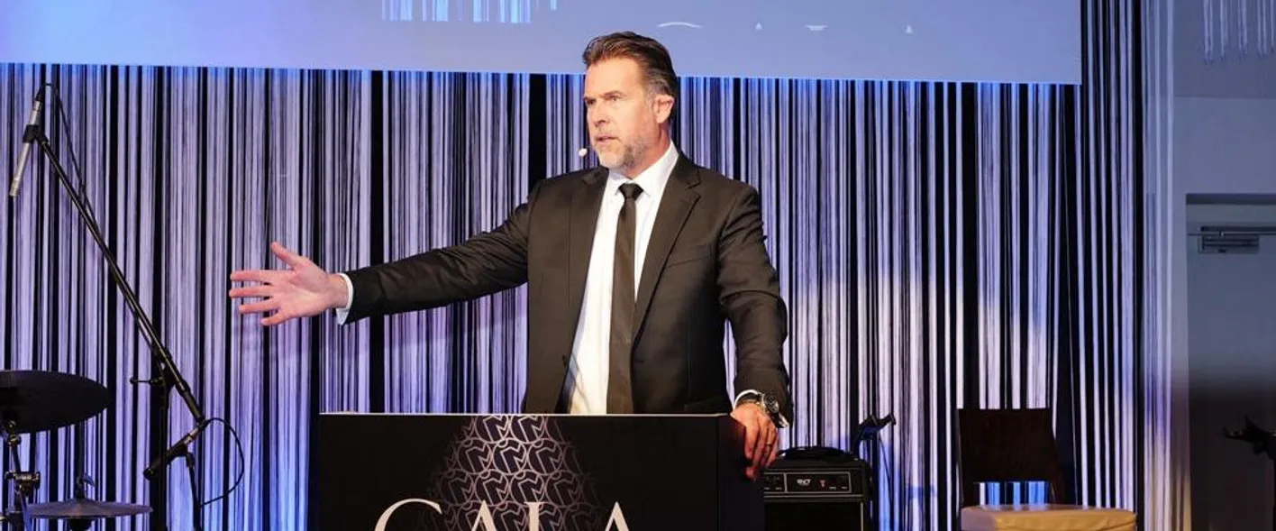 Gala Dinner MC stands at a plinth speaking. He's wearing a suit.