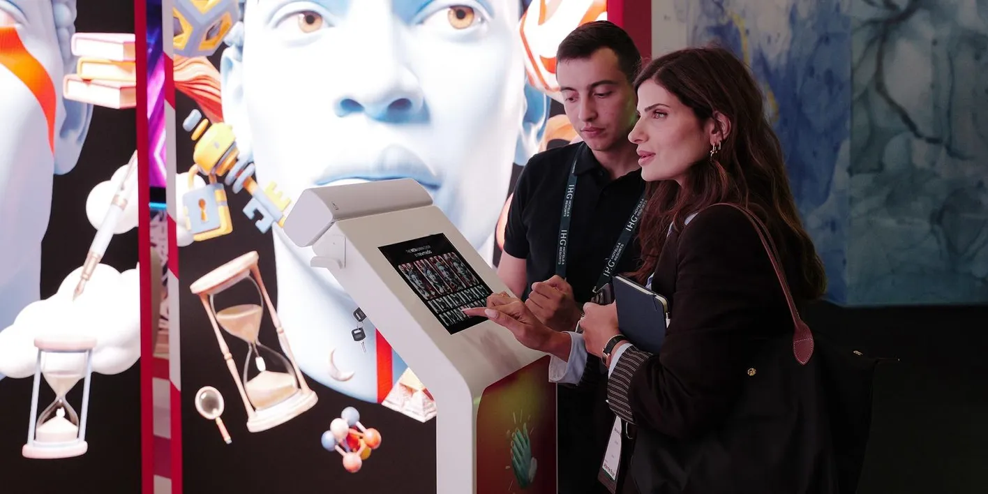 IMEX attendees stan looking at a touch screen with a mural of a person in the background.