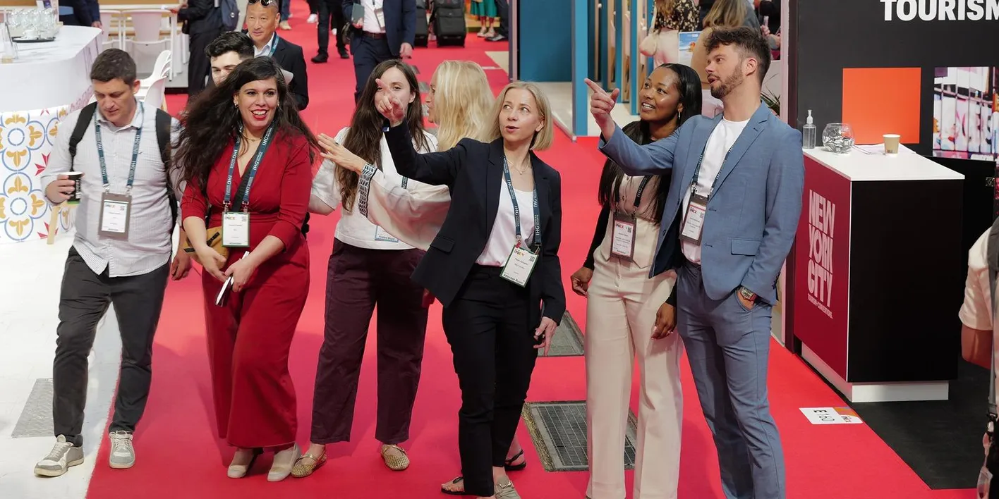 A group of buyers gathered on the show floor pointing and looking up at the hall aisle
