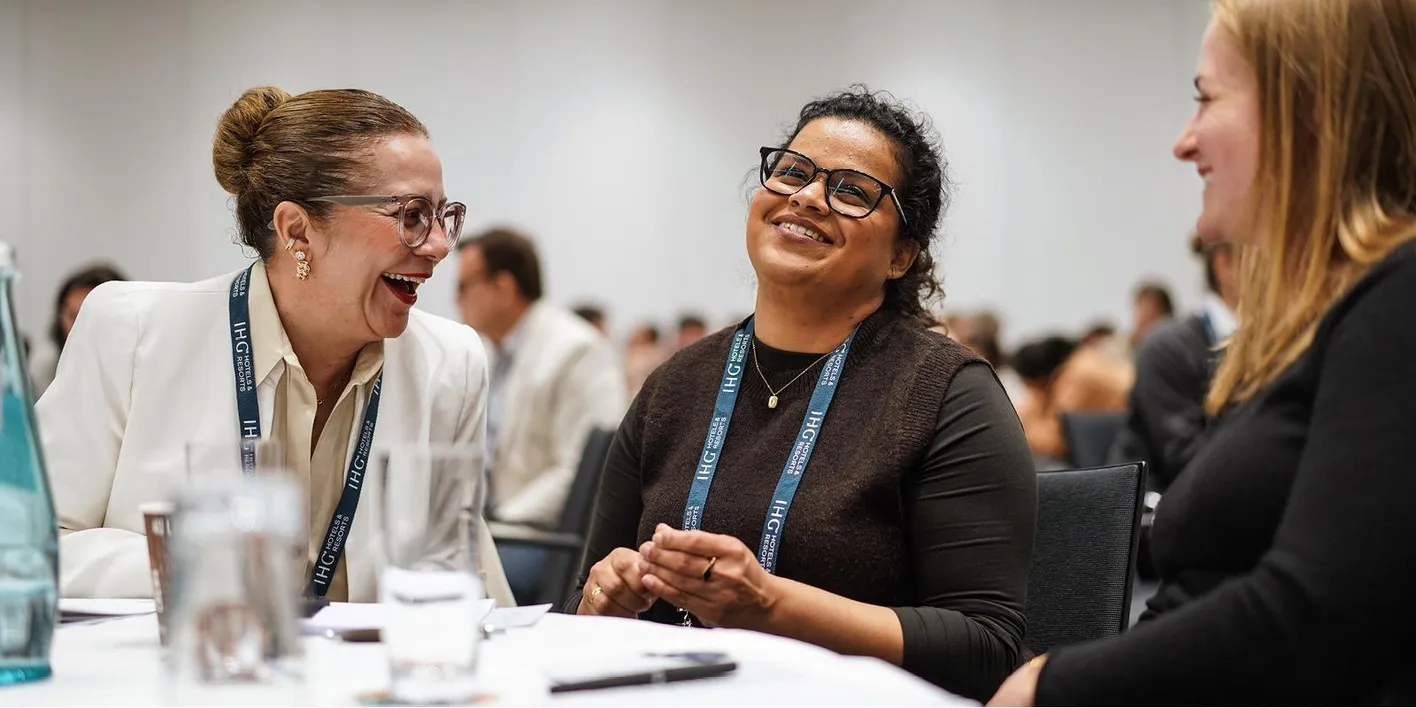 Three women sit on tables talking and smiling during IMEX Frankfurt's Exclusively Corporate