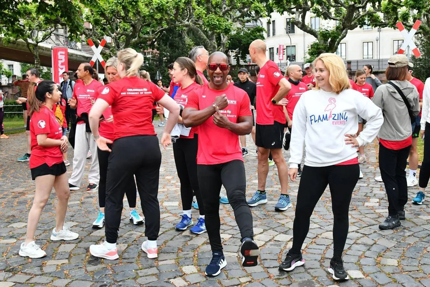 Stretching session before the IMEXrun event, one man is wearing sunglasses pointing to his bracelet