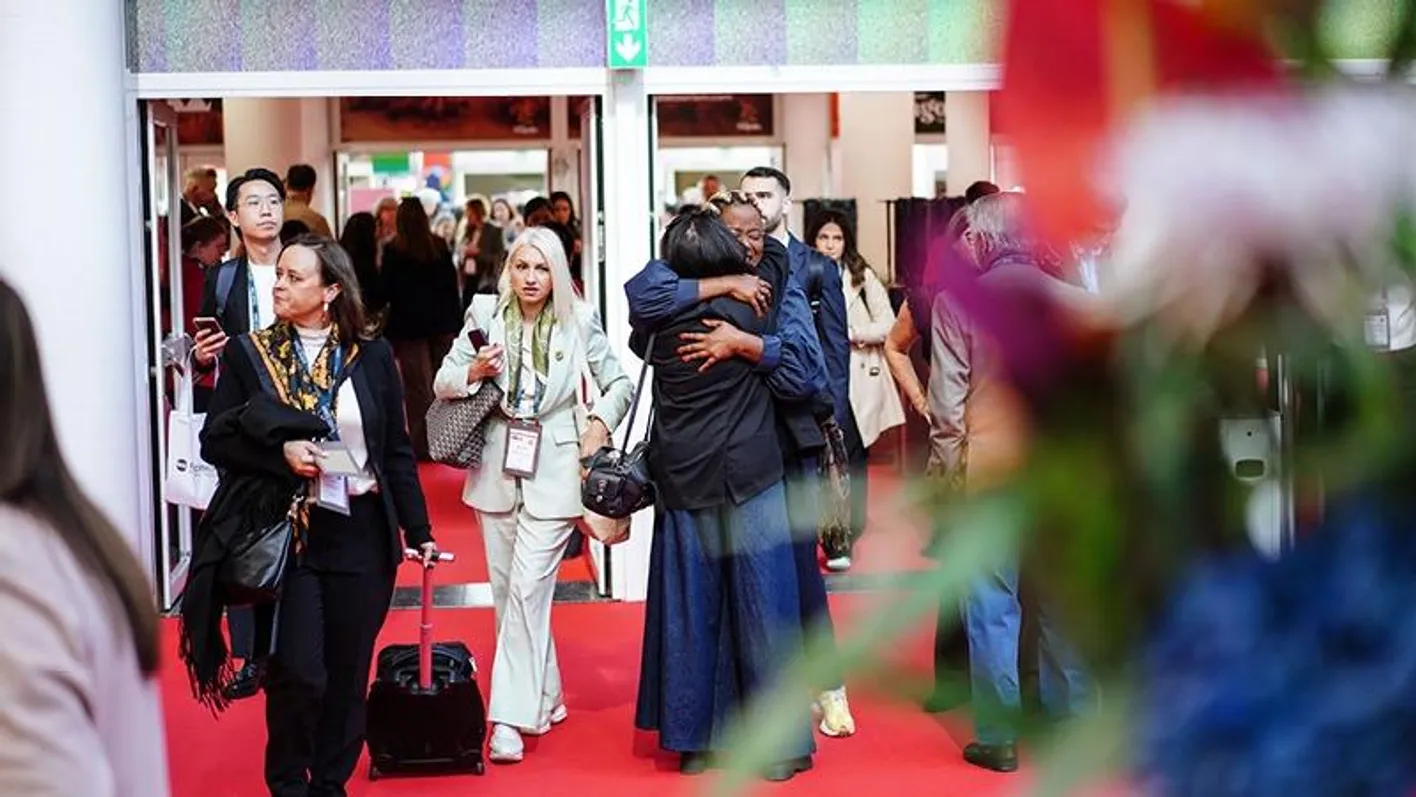 Two attendees hug on IMEX Frankfurt's show floor by the Hall 8 entrance.