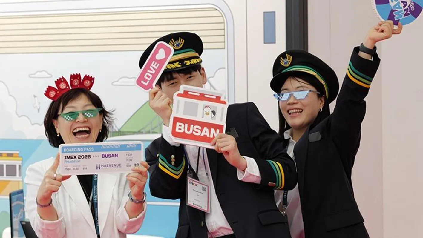 A group of exhibitors smiling on at IMEX. All of them are holding fun stickers and wearing hats.