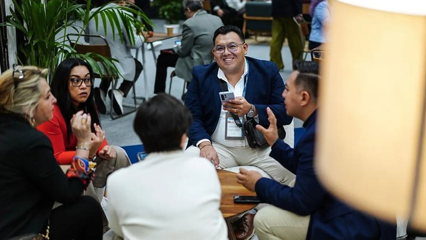 A small group gathered around a low table conversing, one man is looking at the camera smiling