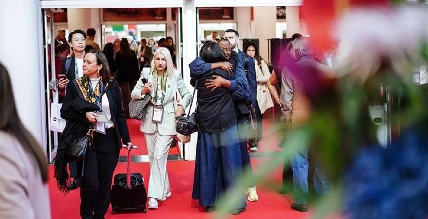 Two attendees hugging each other by the entrance of Hall 8, other attendees are walking past them