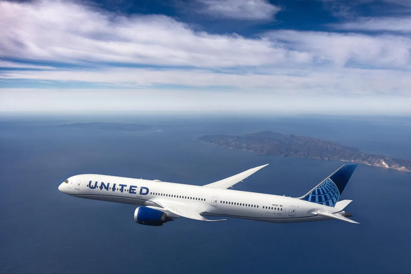 United for business plane flying over the sea with an island in the background