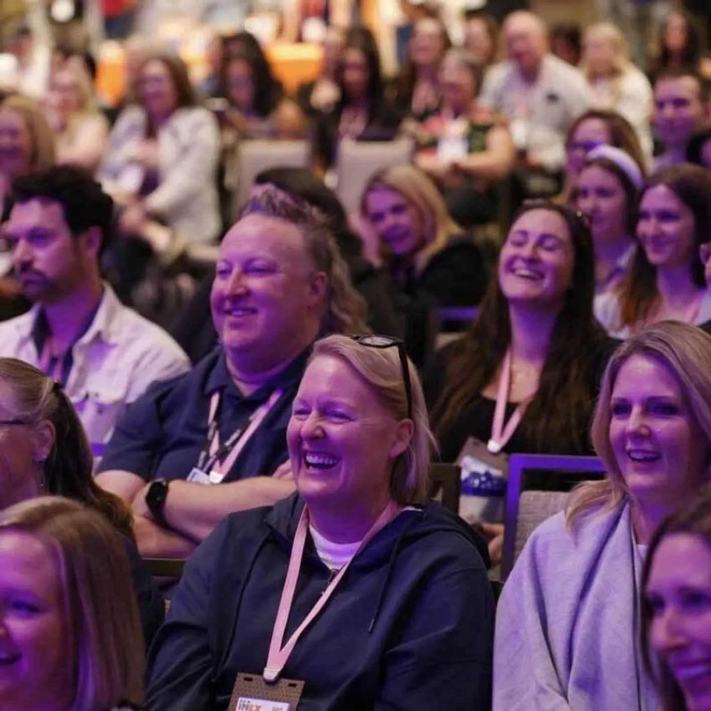 Audience members facing the stage smiling and listening to an education session