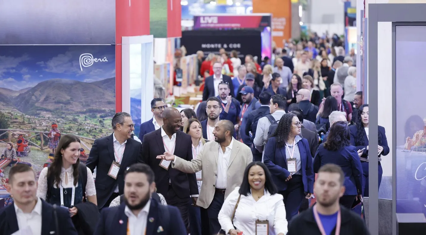 A crowd of attendees facing the camera, walking in a busy aisle in the exhibit hall.