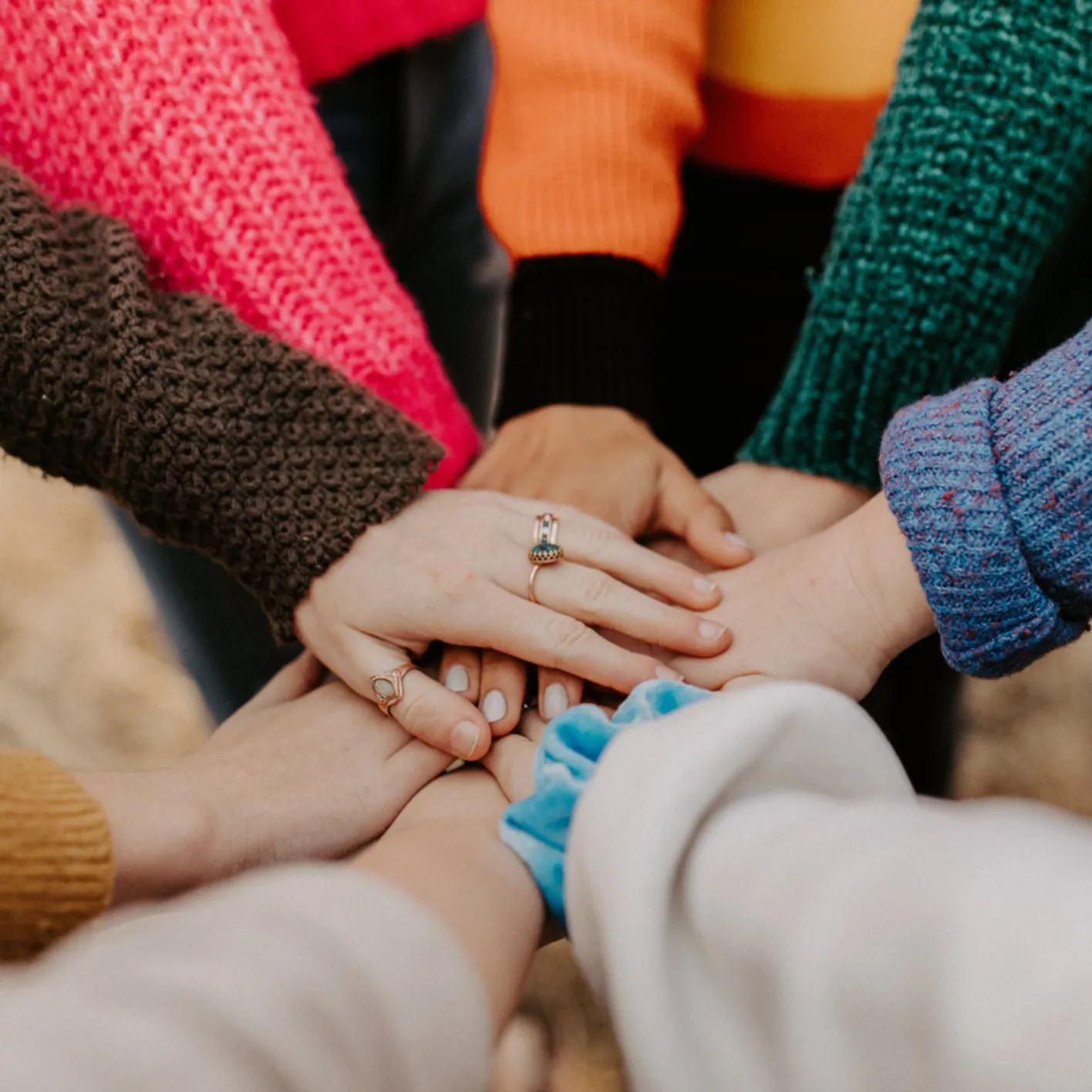Stacked circle of hands comprised of many different people. The top hand has three rings on it.