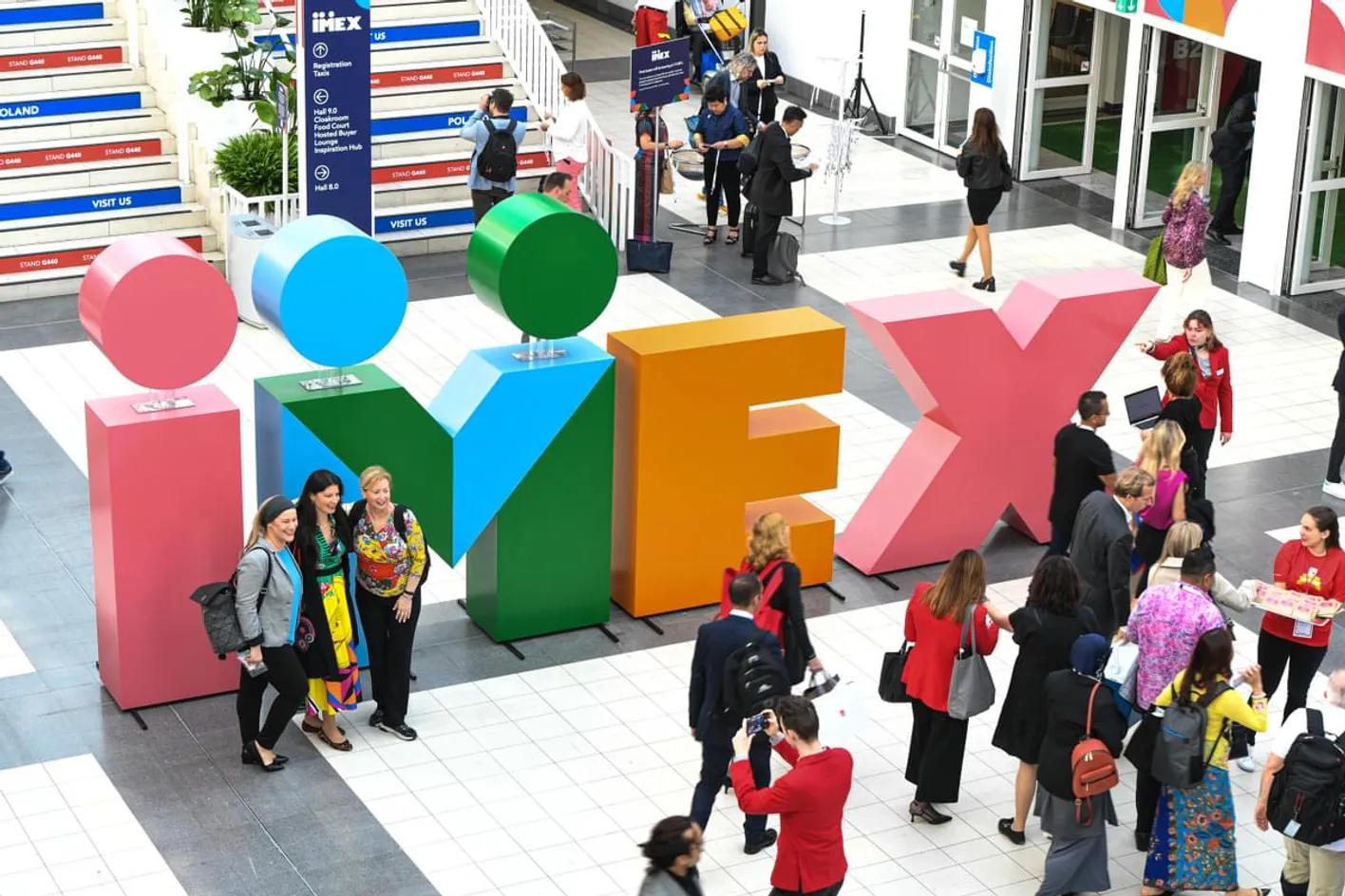 Attendees at IMEX Frankfurt near colorful IMEX letters in Messe Frankfurt's Galleria