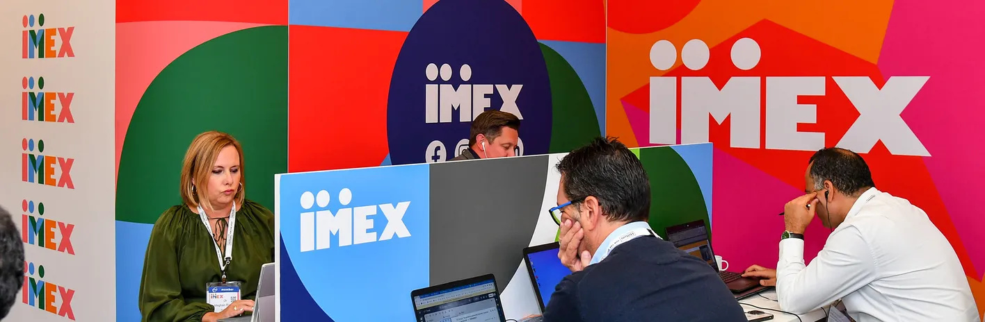  Pressezentrum der IMEX Frankfurt mit gebrandeter Wand und Personen mit ihren Laptops. 