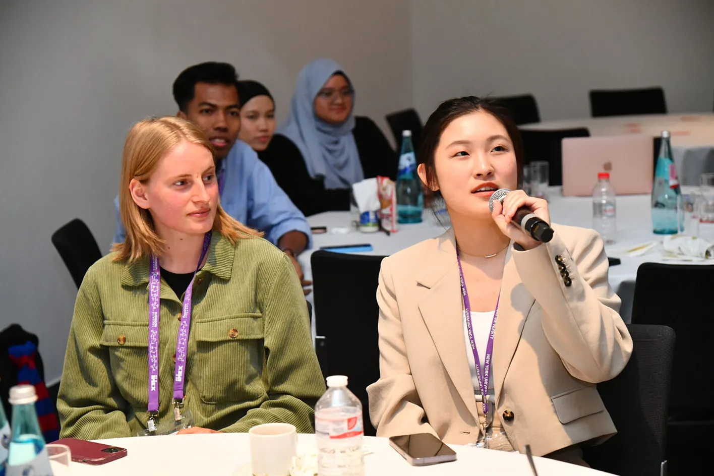 Forum attendees seated at tables with one person speaking into a microphone.