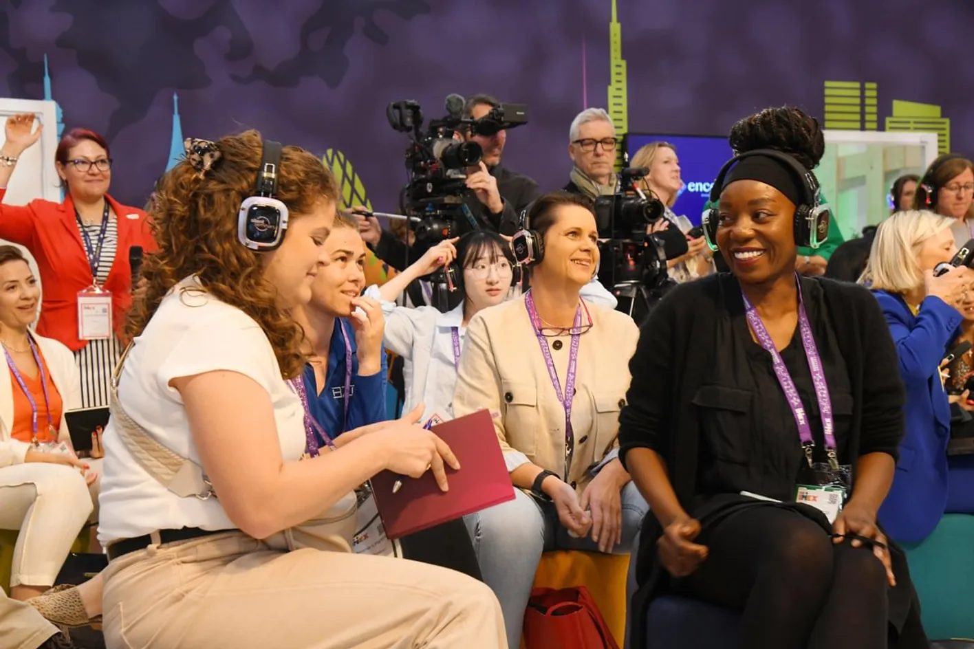 Two attendee seated with headphones at an education session. A camera crew is filming in background