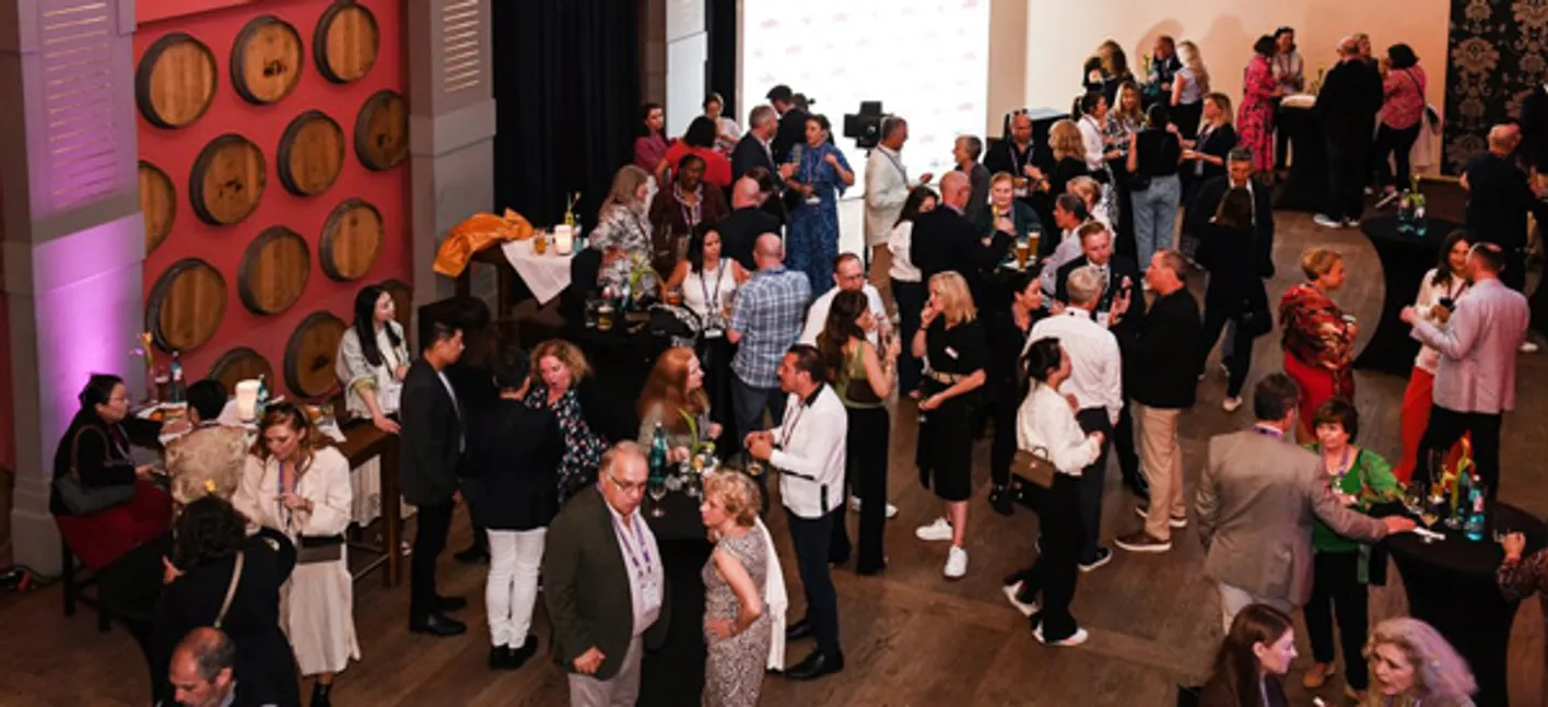 A crowd of people at a social event. They holding drinks and talking to each other.