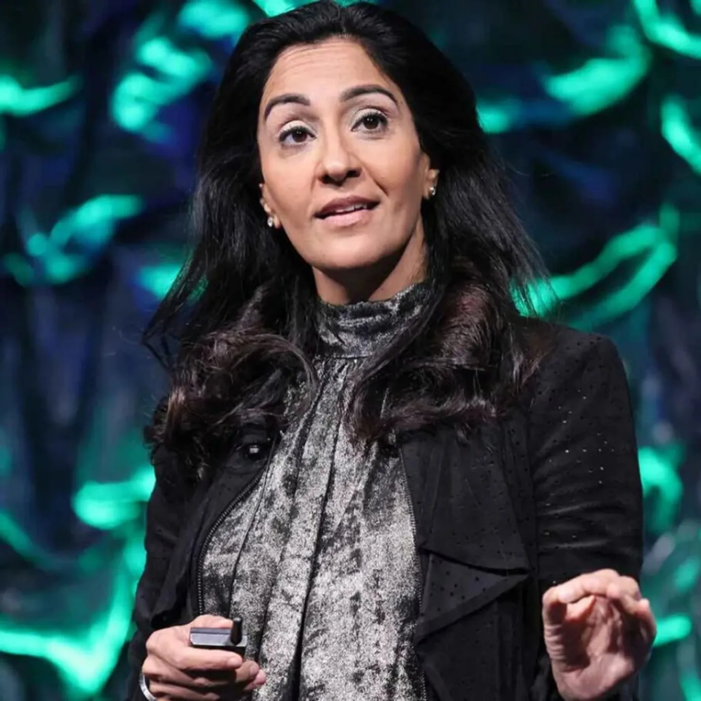 Person with long dark hair gesturing in front of green and blue abstract background