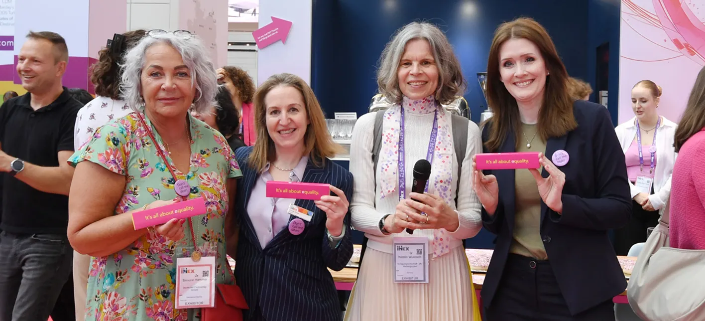 4 attendees stand smiling at the camera holding small pink signs that read 'It's all about equality'