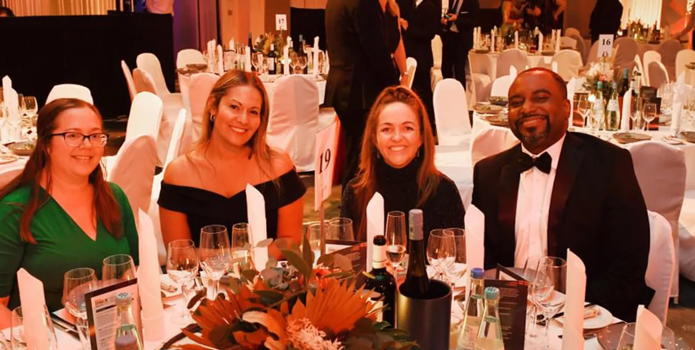 Gala Dinner attendes sit at a table in formal dress smiling at the camera