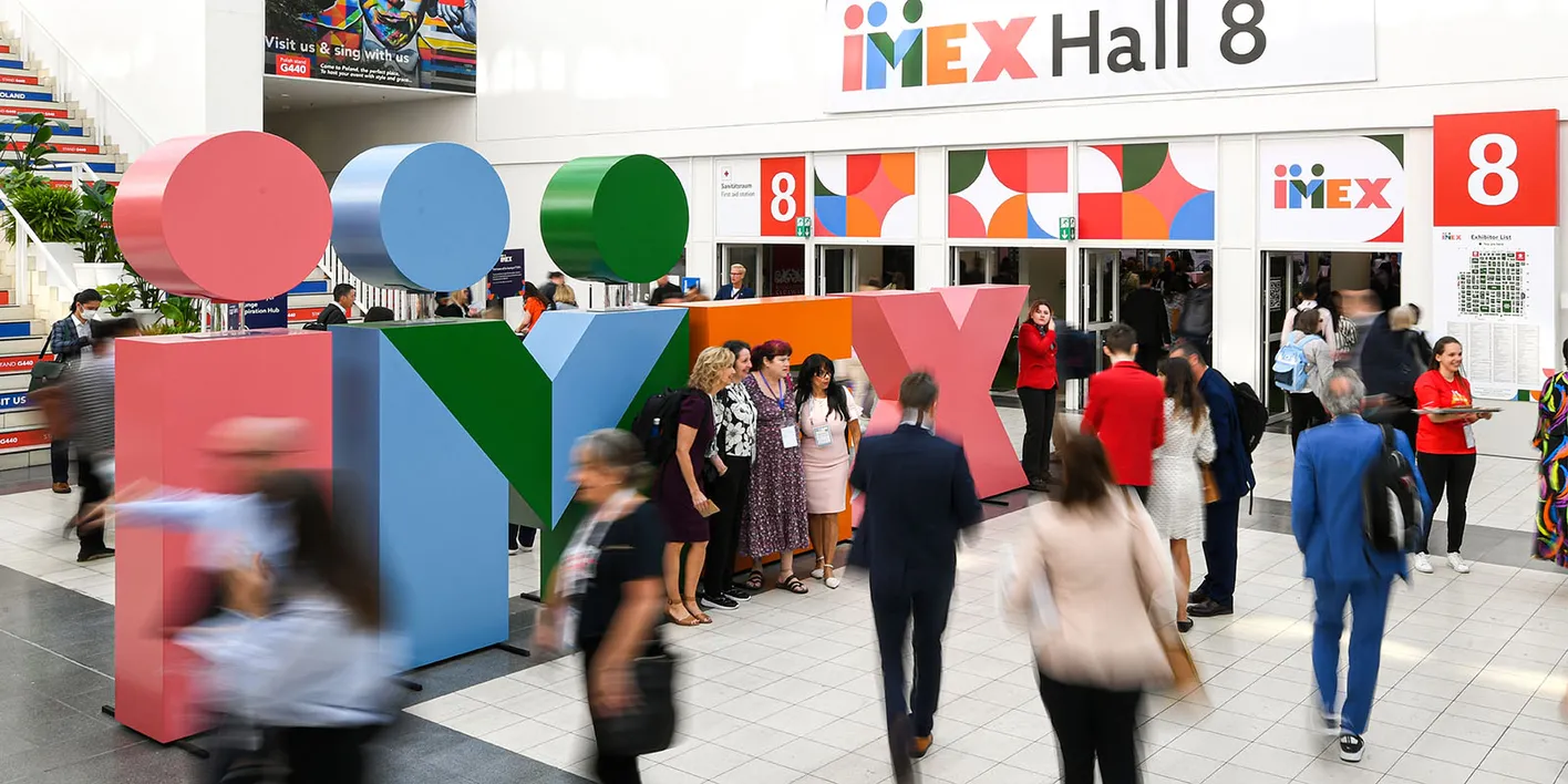 Crowds at IMEX Frankfurt's Hall 8 entrance with colorful signage and geometric shapes on banners.
