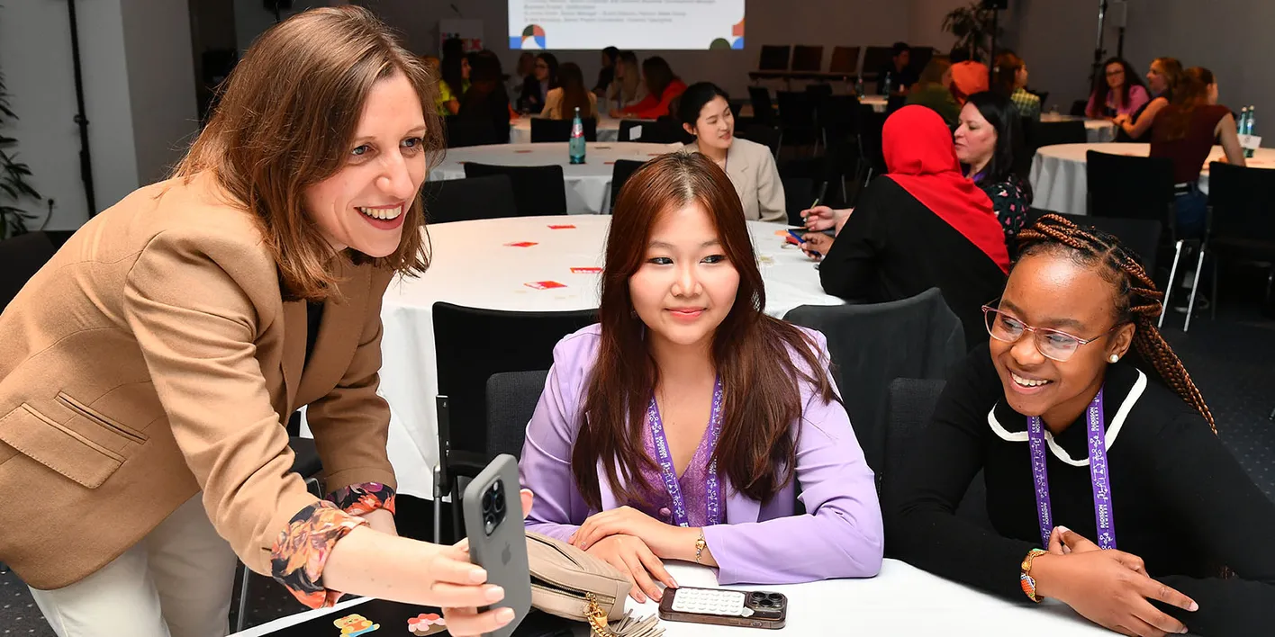 Attendees at IMEX Frankfurt seated at round tables, discussing and viewing content on a phone.