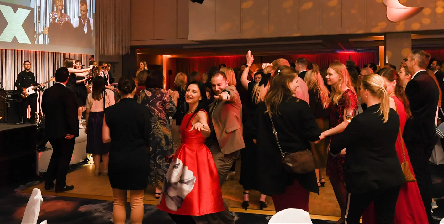 A large crowd of IMEX attendees dancing at the Gala Dinner. 2 attendees look and point at the camera