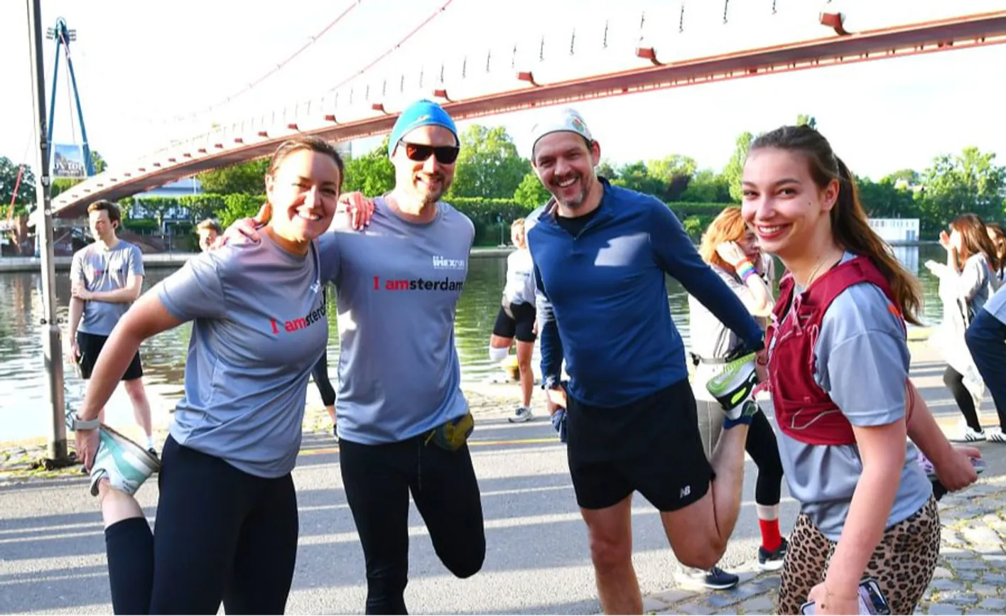Two men and two women in exercise clothes smile at the camera stretching before the IMEXrun.