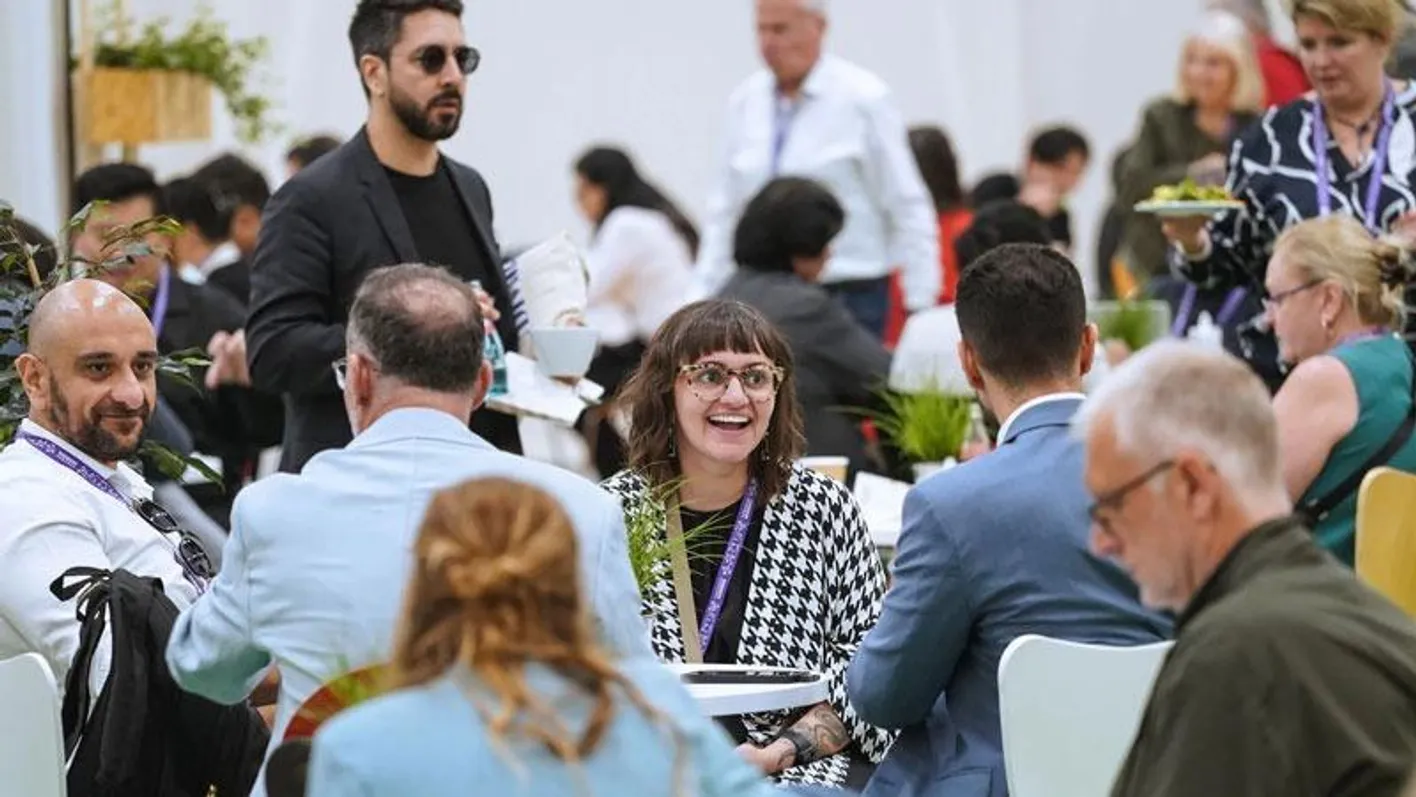 A crowd of IMEX attendees sitting at tables. One attendee looks beyond the camera smiling