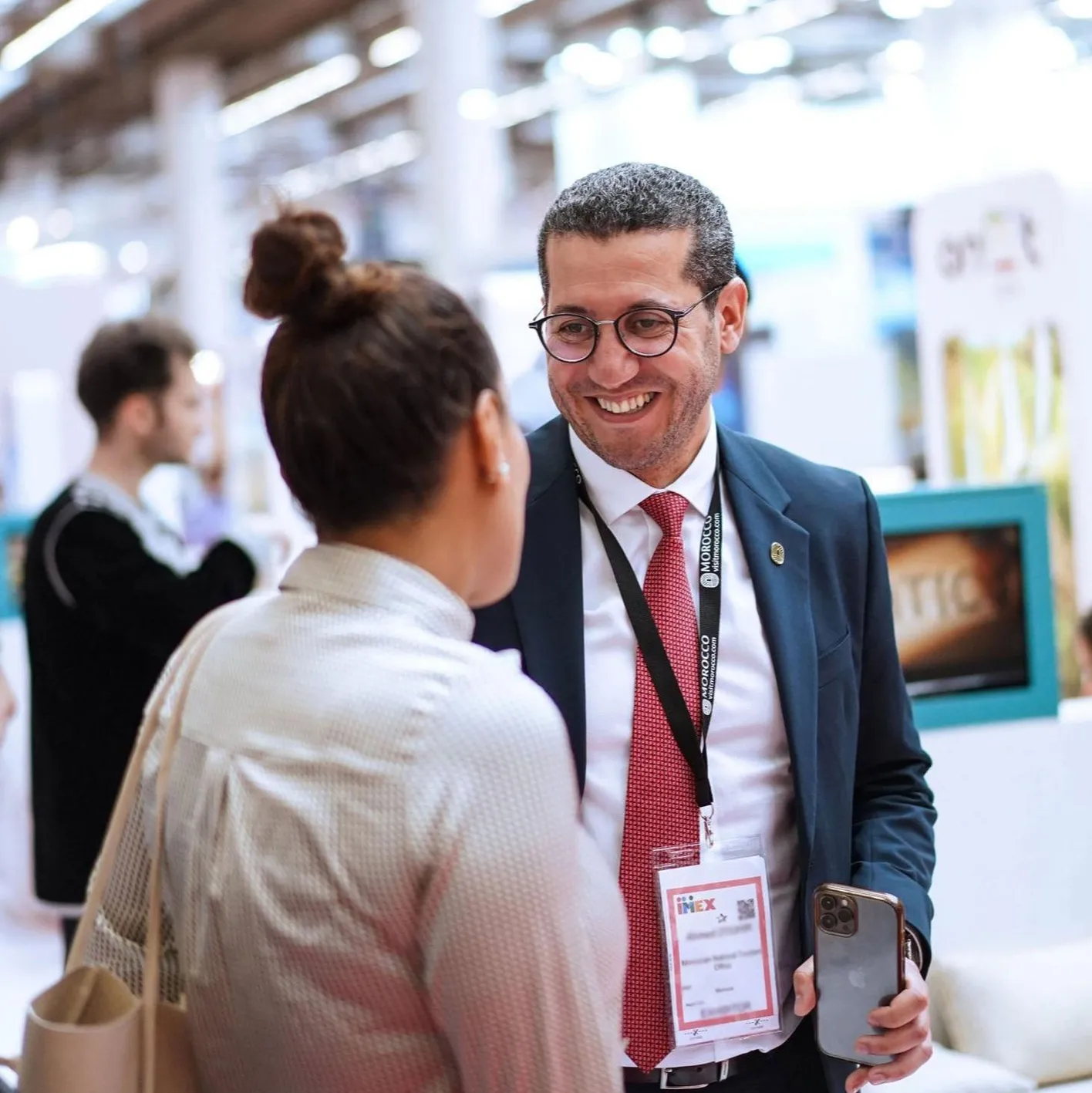 Two attendees stand on the show floor. One has their back to the camera, the other is smiling at her