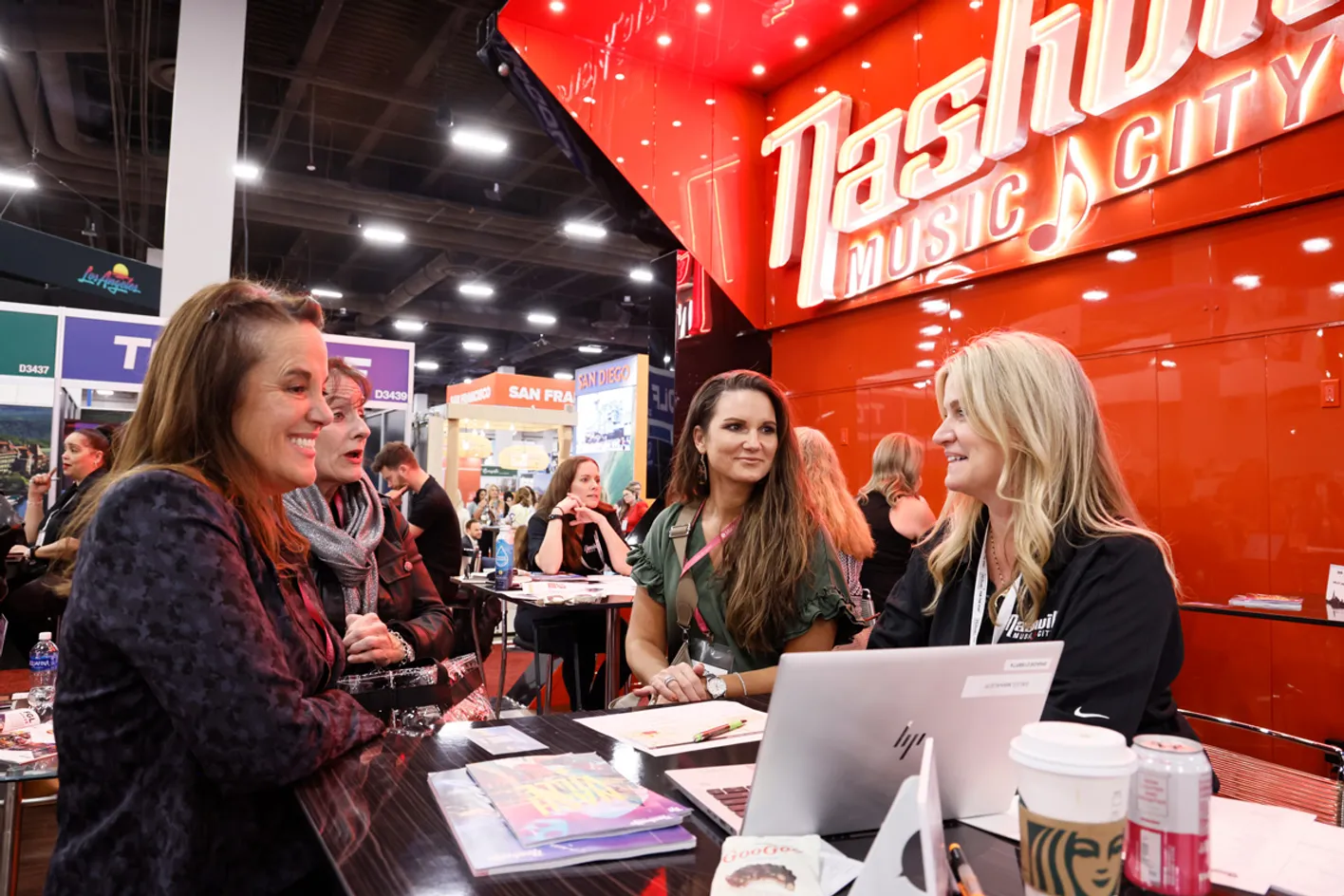 People gathered around a booth at IMEX, engaging with screens.