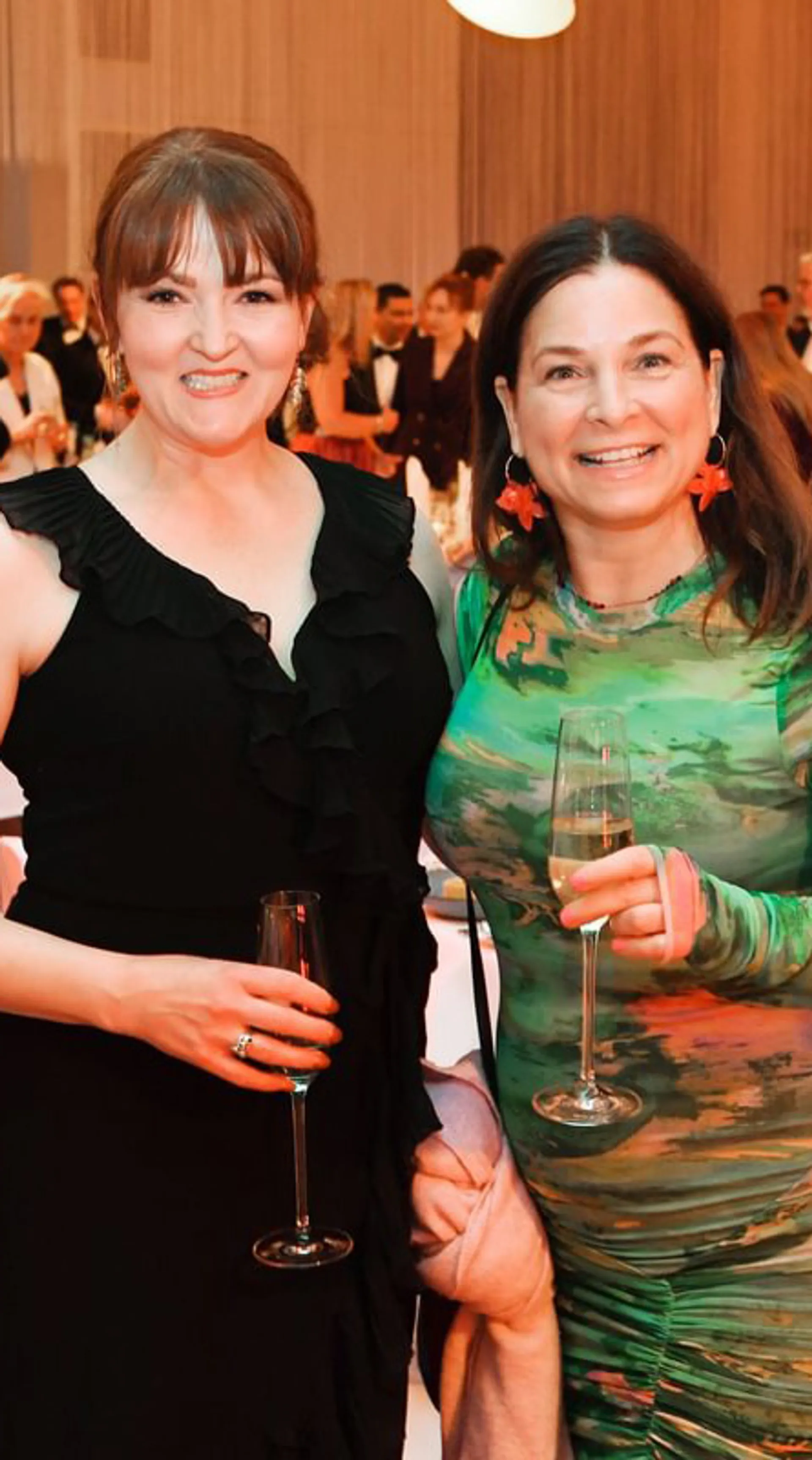Two attendees in formal dress smiling at the camera holding champagne glasses