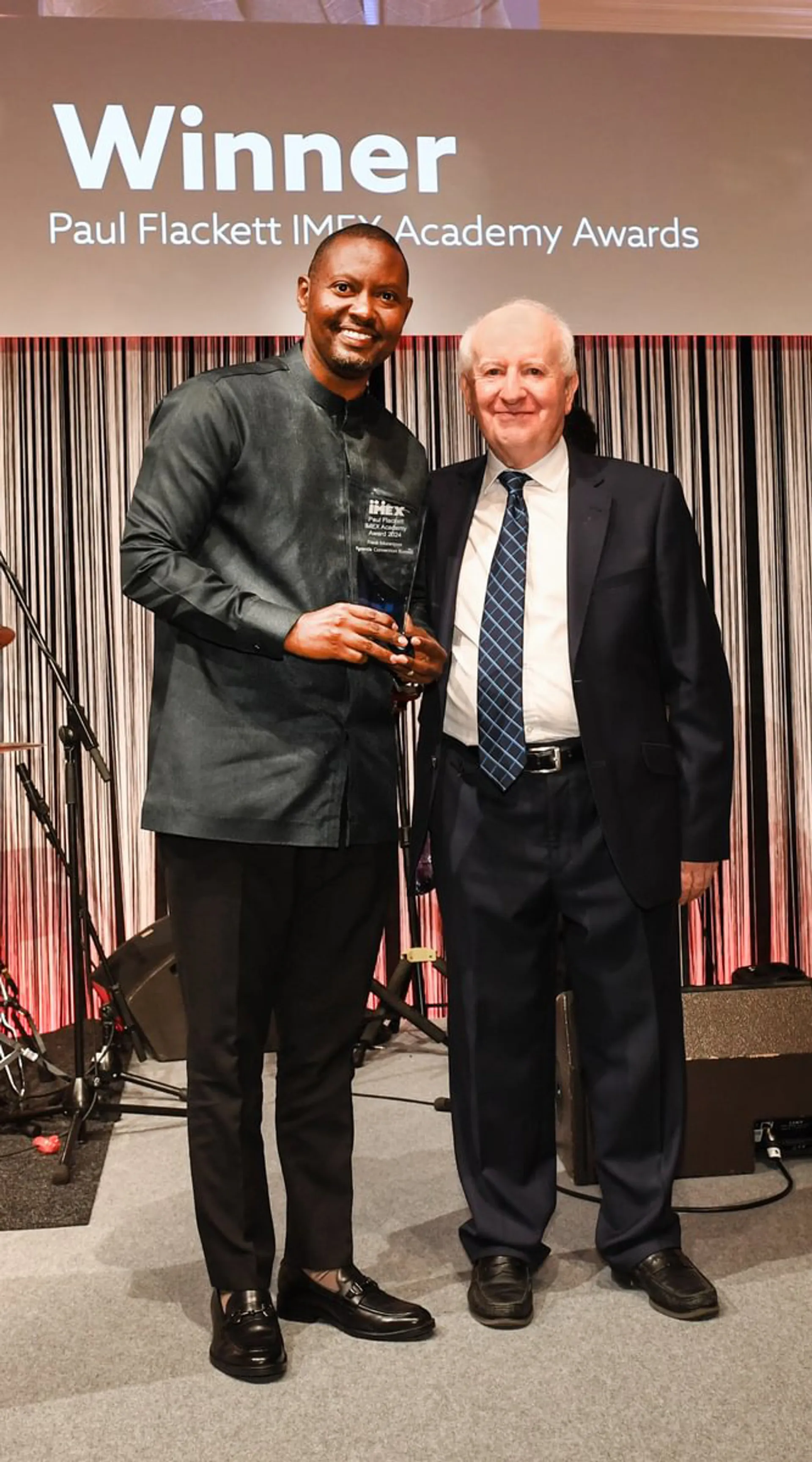 An award winner stands smiling alongside IMEX Chairman Ray Bloom