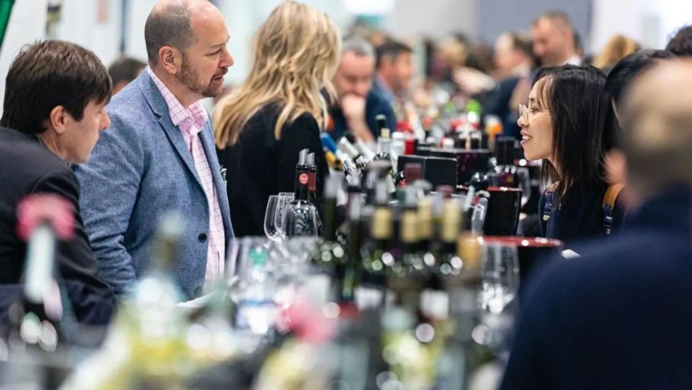 A woman is talking to a man. One is an exhibitor while the other is a visitor. Between them, bottles